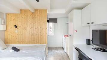 Un dormitorio con cabecera de madera, cama con cubrecama a rayas, mesita de noche con lámpara y televisor sobre un mueble blanco.