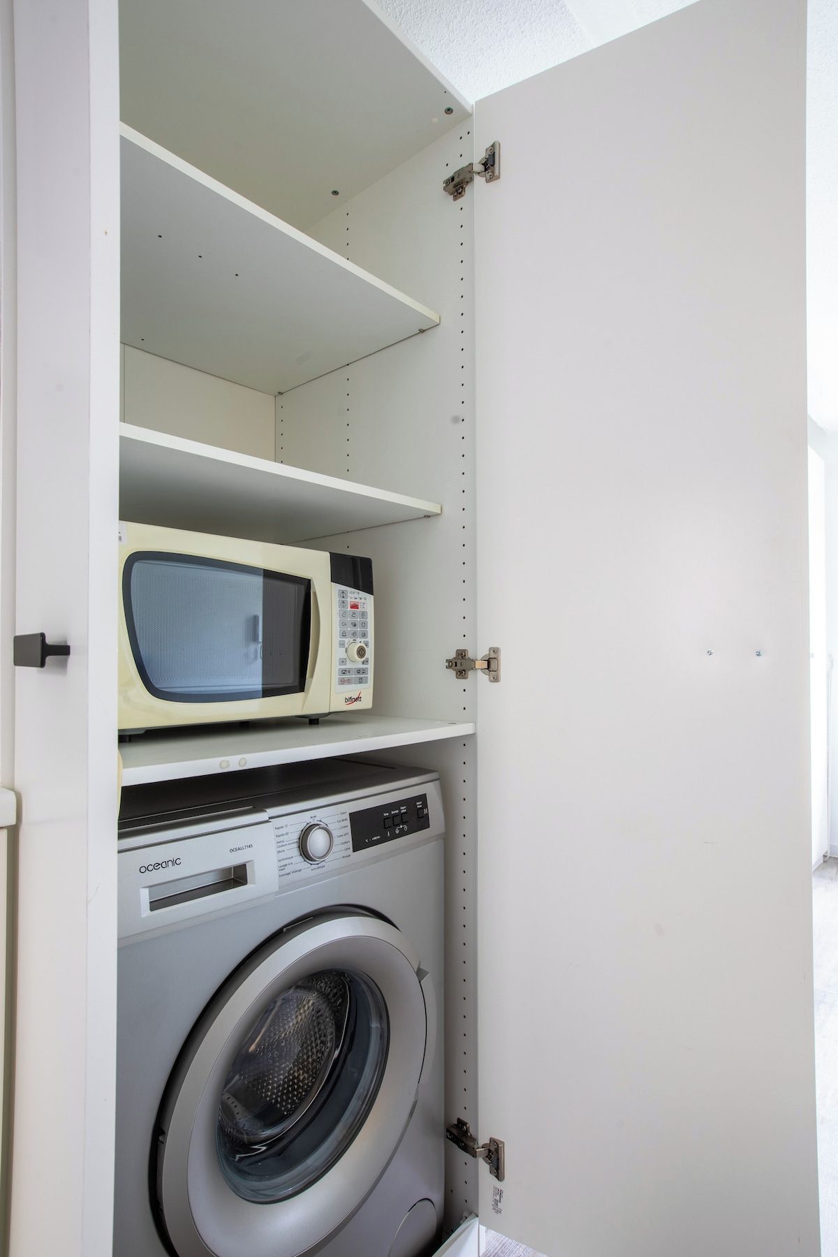 Une buanderie équipée d’un lave-linge, d’un four à micro-ondes et d’une étagère.