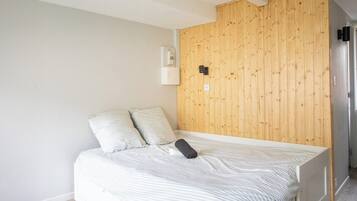 Una cama individual con ropa de cama a rayas, un panel de pared de madera, una mesita de noche blanca y un interruptor negro.
