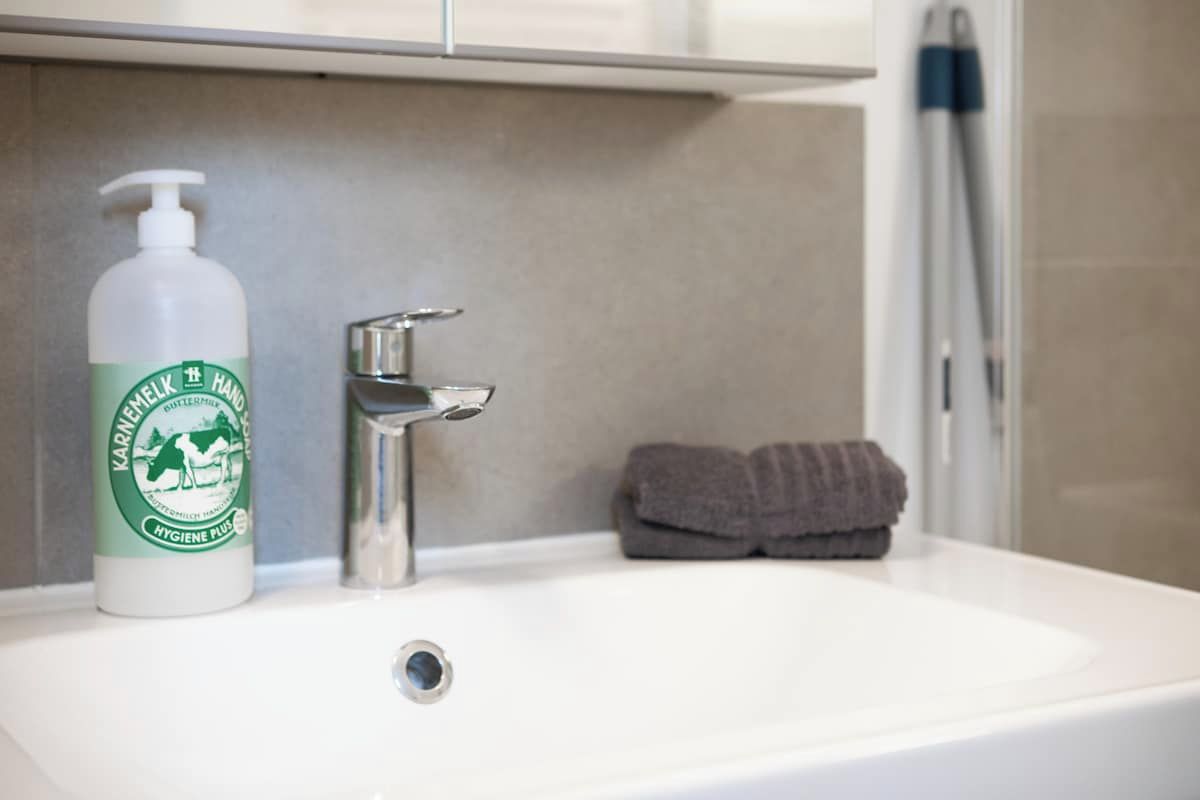 Un lavamanos con una botella de jabón Karolinen Hand Hygiene Plus, un grifo y una toalla.