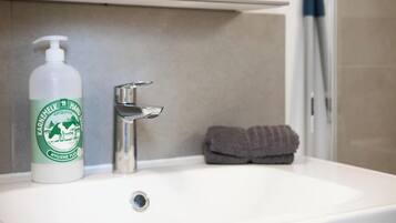 Un lavamanos con una botella de jabón Karolinen Hand Hygiene Plus, un grifo y una toalla.