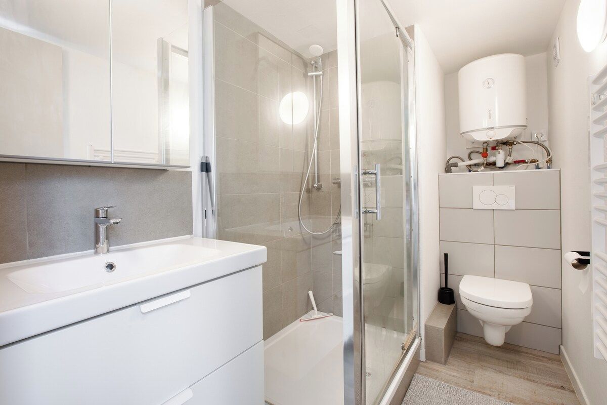 Een moderne badkamer met een douche met glazen wand, een witte wastafel en een toilet.