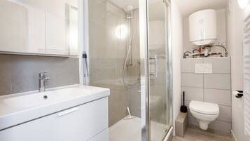 Een moderne badkamer met een douche met glazen wand, een witte wastafel en een toilet.