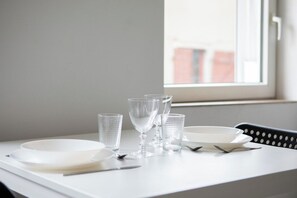 Een tafel gedekt met witte borden, heldere glazen en bestek, vlakbij een raam met uitzicht op gebouwen.