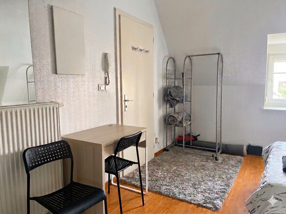 Una habitación pequeña con una cama, un escritorio, una silla, un radiador y una ventana.