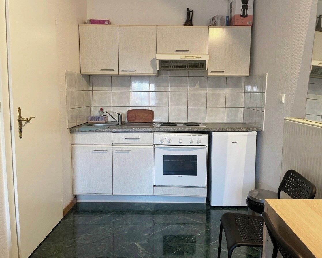 Une cuisine compacte avec des meubles blancs, un four encastré et un petit réfrigérateur.