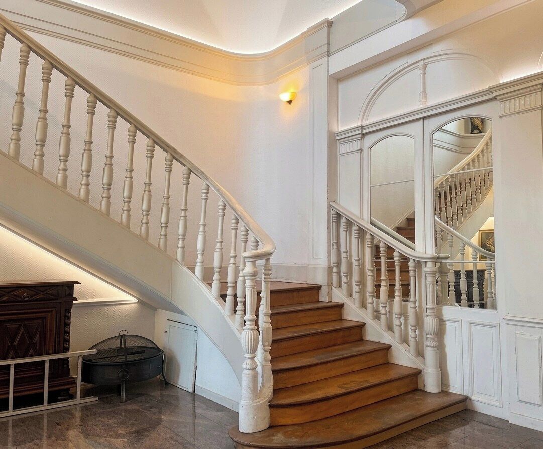 Un grand escalier avec des balustrades blanches et des marches en bois, menant à l’étage supérieur.