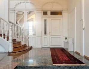Een statige trap met witte balustrades die uitkomt op een vloer met een rode loper.