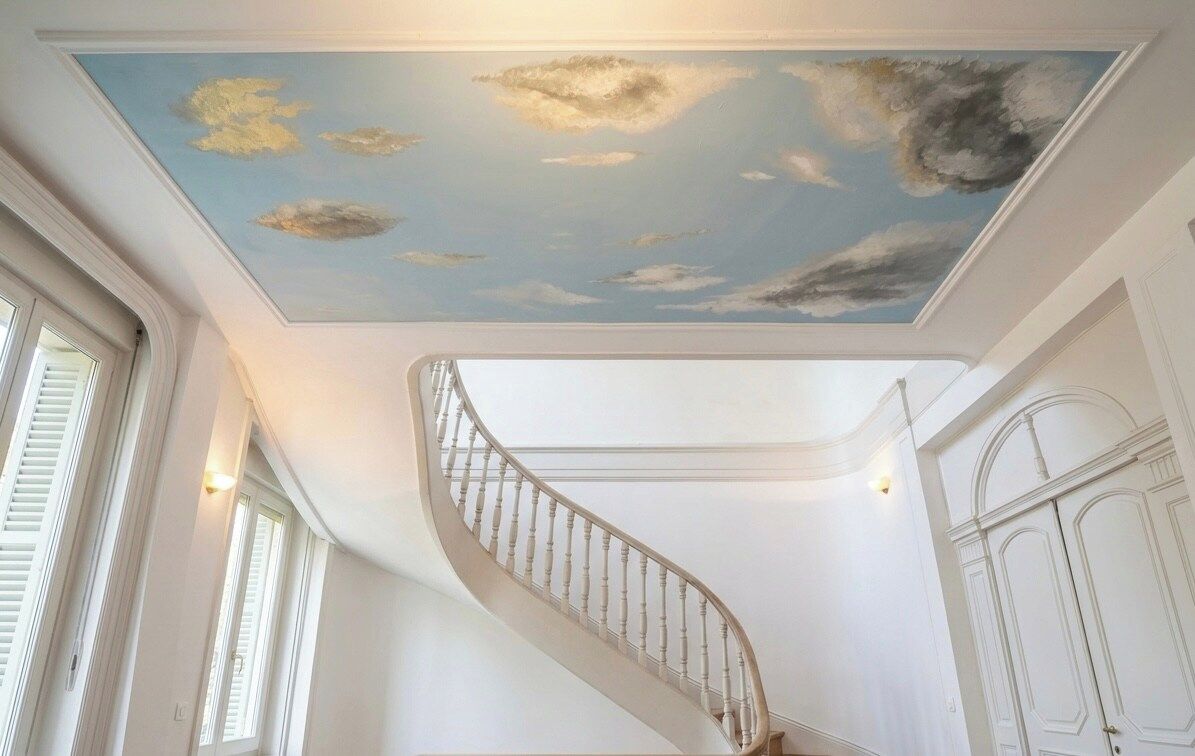 Una escalera en espiral con un techo pintado que representa nubes.