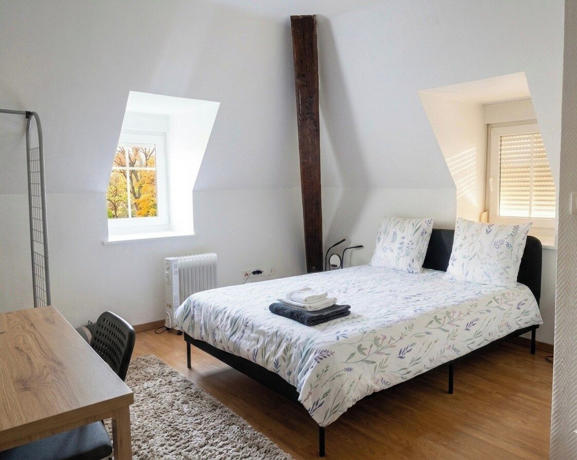 Une chambre à coucher avec un lit, un bureau, un radiateur et une fenêtre.