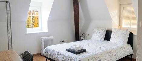 Een slaapkamer met een bed, bureau, radiator en raam.