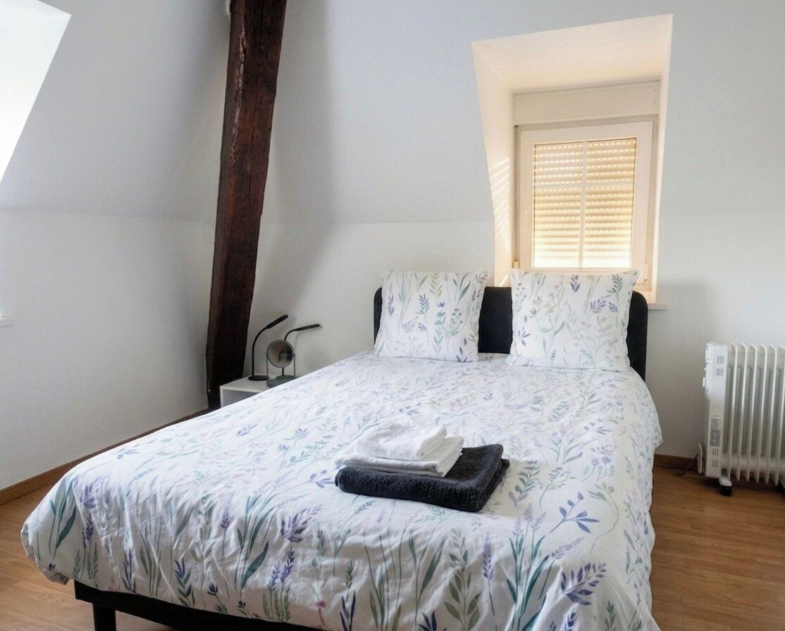 Une chambre à coucher avec un lit, une fenêtre avec des stores, un radiateur et une table de chevet.