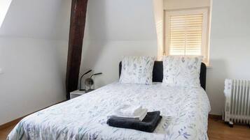 Une chambre à coucher avec un lit, une fenêtre avec des stores, un radiateur et une table de chevet.