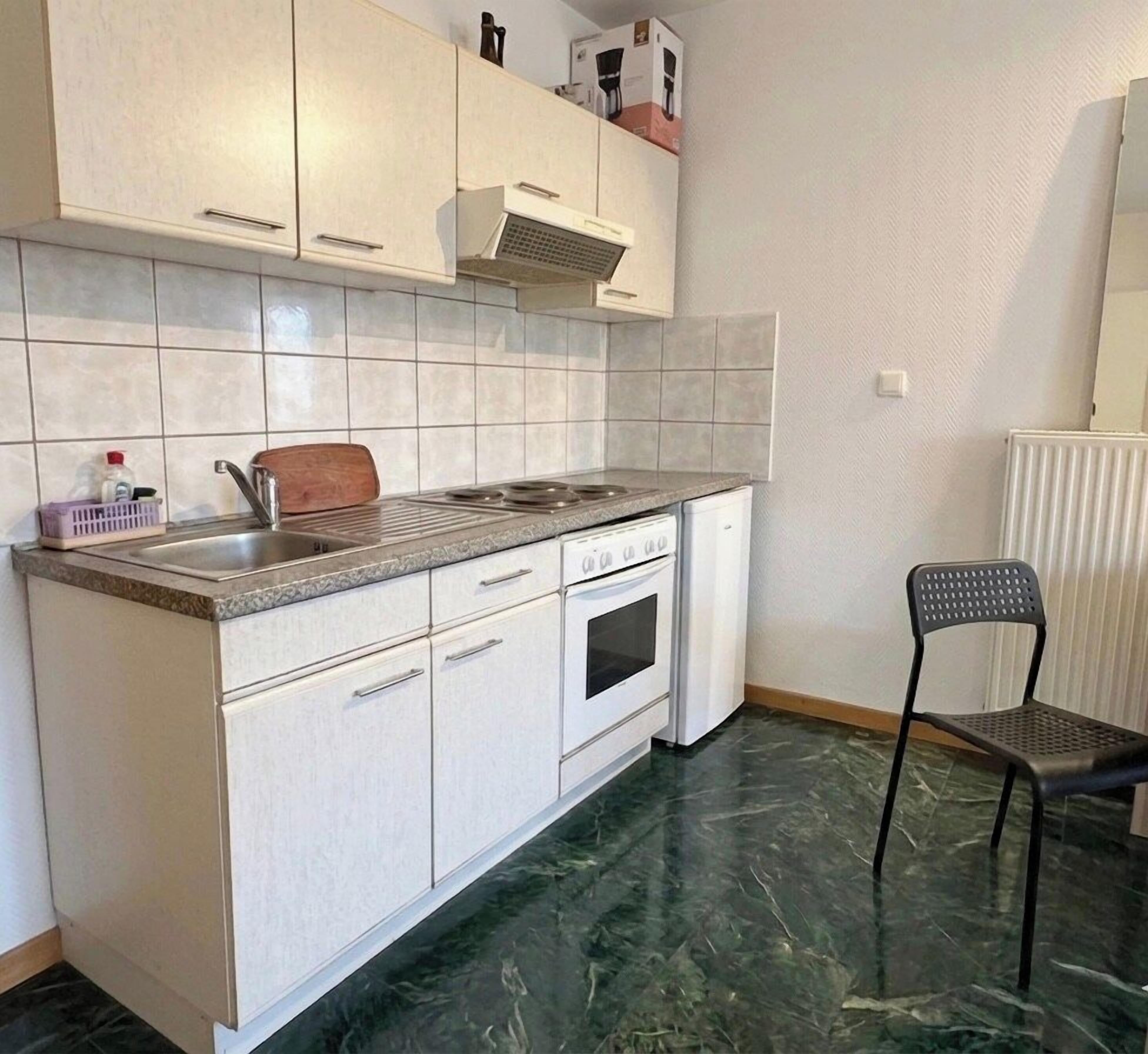 Une cuisine avec des armoires blanches, un évier en acier inoxydable, une cuisinière et une chaise.