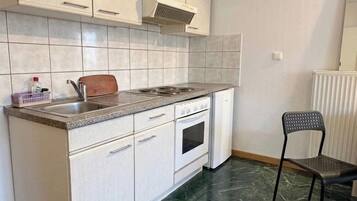 Una cocina con armarios blancos, un lavamanos de acero inoxidable, una estufa y una silla.
