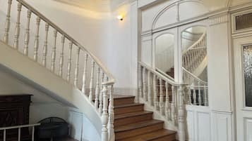 Una imponente escalera con balaustres blancos y peldaños de madera, que conduce a un rellano con un amplio arco de entrada.