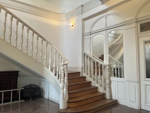Een statige trap met witte balustrades en houten treden, die uitkomt op een plateau met een grote, gewelfde deuropening.