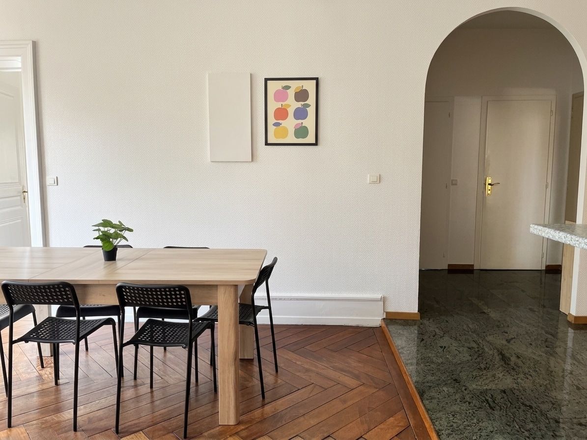 Un coin repas avec une table en bois et quatre chaises, une plante en pot et un tableau encadré au mur.