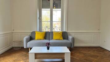 A room with a grey sofa with yellow cushions, a white coffee table, and a herringbone wooden floor.
