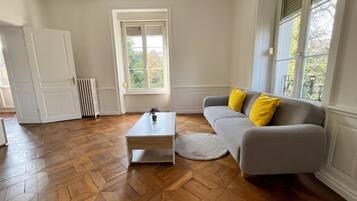 A living room with a herringbone wooden floor, a grey sofa with yellow cushions, a white coffee table, and a radiator.