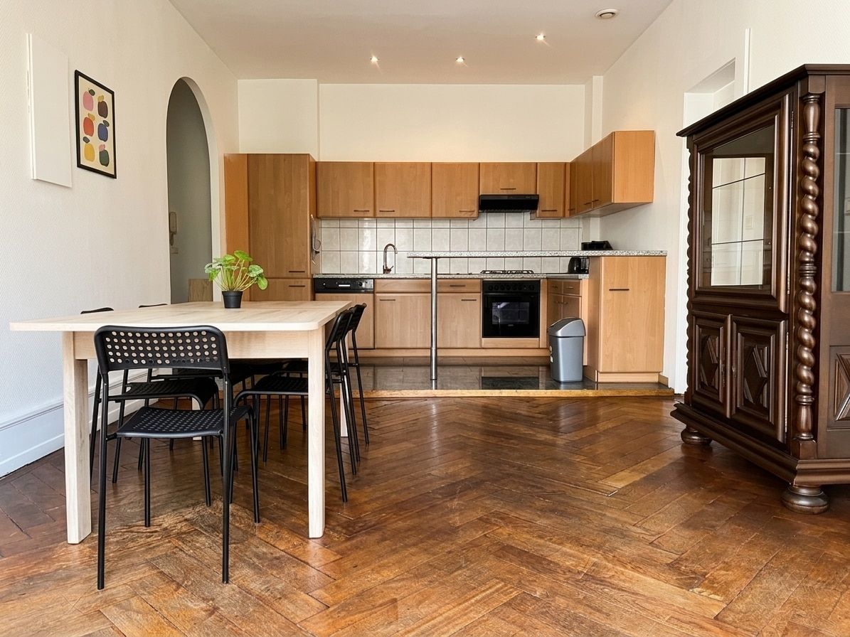 Une cuisine moderne avec des meubles en bois, une table à manger avec des chaises et un parquet disposé en motif chevron.