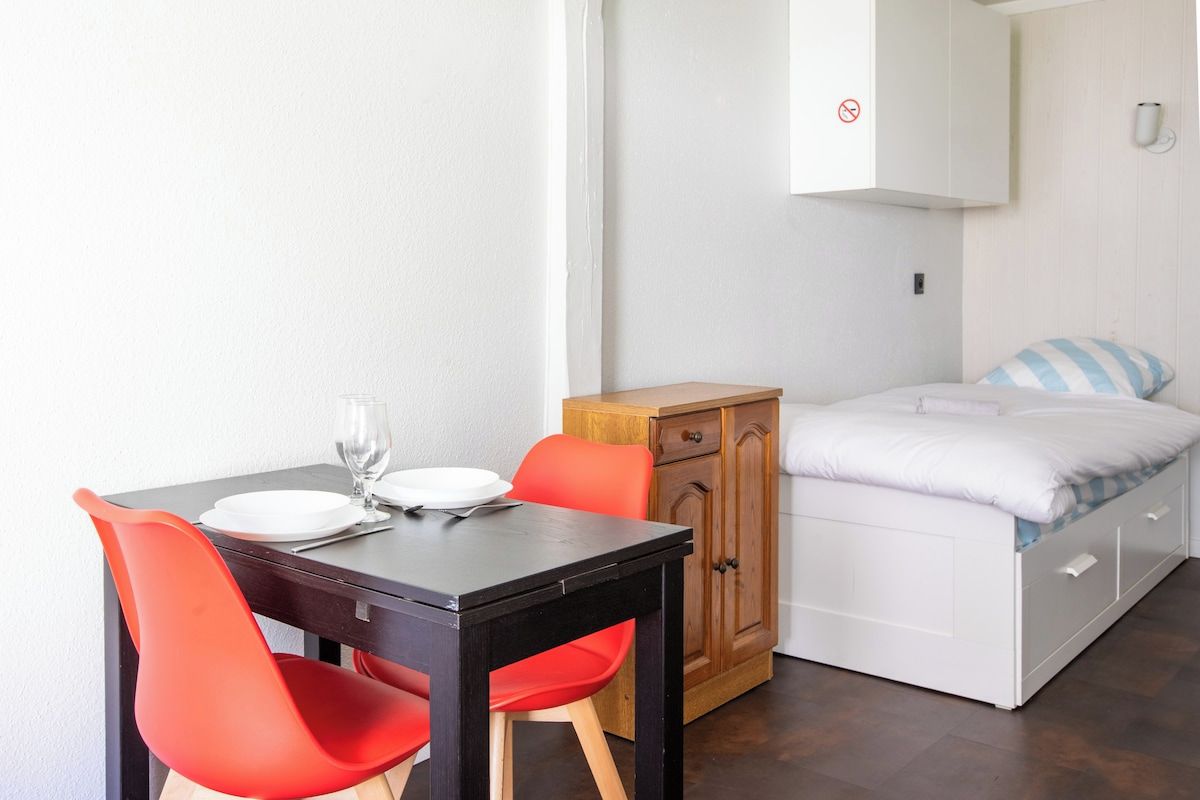 Una habitación pequeña con una cama, un armario de madera y una mesa con sillas.