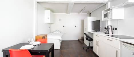 A compact room with a bed, a dining table with chairs, a kitchenette, and a small bathroom.