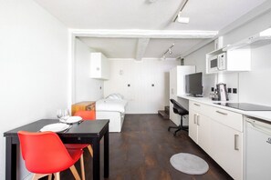 Een compacte kamer met een bed, een eettafel met stoelen, een kitchenette en een kleine badkamer.