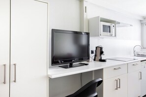 Een moderne keuken met een flatscreen televisie, magnetron en koffieapparaat op het aanrecht.