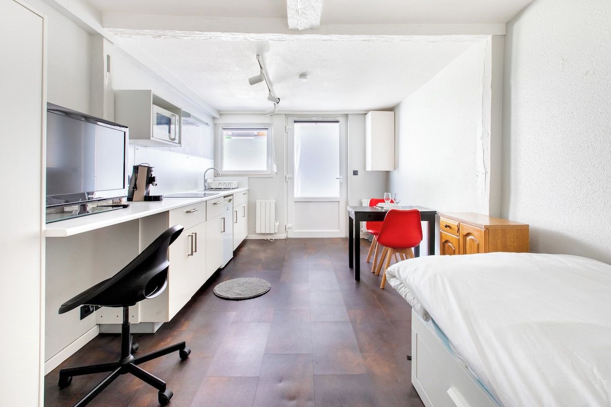 Una habitación de hotel compacta con cama, escritorio con silla, kitchenette y baño.