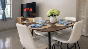 Zona pranzo con un tavolo apparecchiato per quattro persone, un vaso di fiori e una televisione che mostra il logo Netflix.