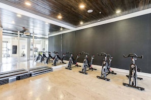Un gimnasio con bicicletas estáticas dispuestas en fila, suelo pulido y pared oscura.