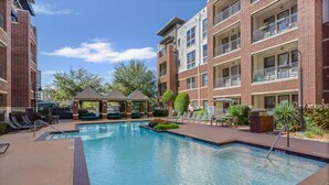 A swimming pool with lounge chairs and a gazebo, surrounded by brick buildings with balconies.