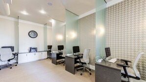 Un moderno spazio ufficio con pareti divisorie in vetro, diverse postazioni di lavoro e una sveglia al muro.