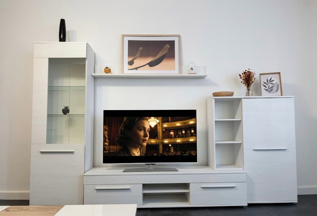 Un salon moderne avec un téléviseur à écran plat fixé sur un meuble blanc, un meuble vitré et une petite plante.