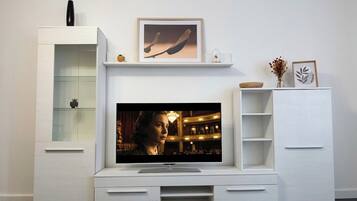 Een moderne woonkamer met een flatscreen televisie, bevestigd aan een wit tv-meubel, een glazen kast en een kleine plant.