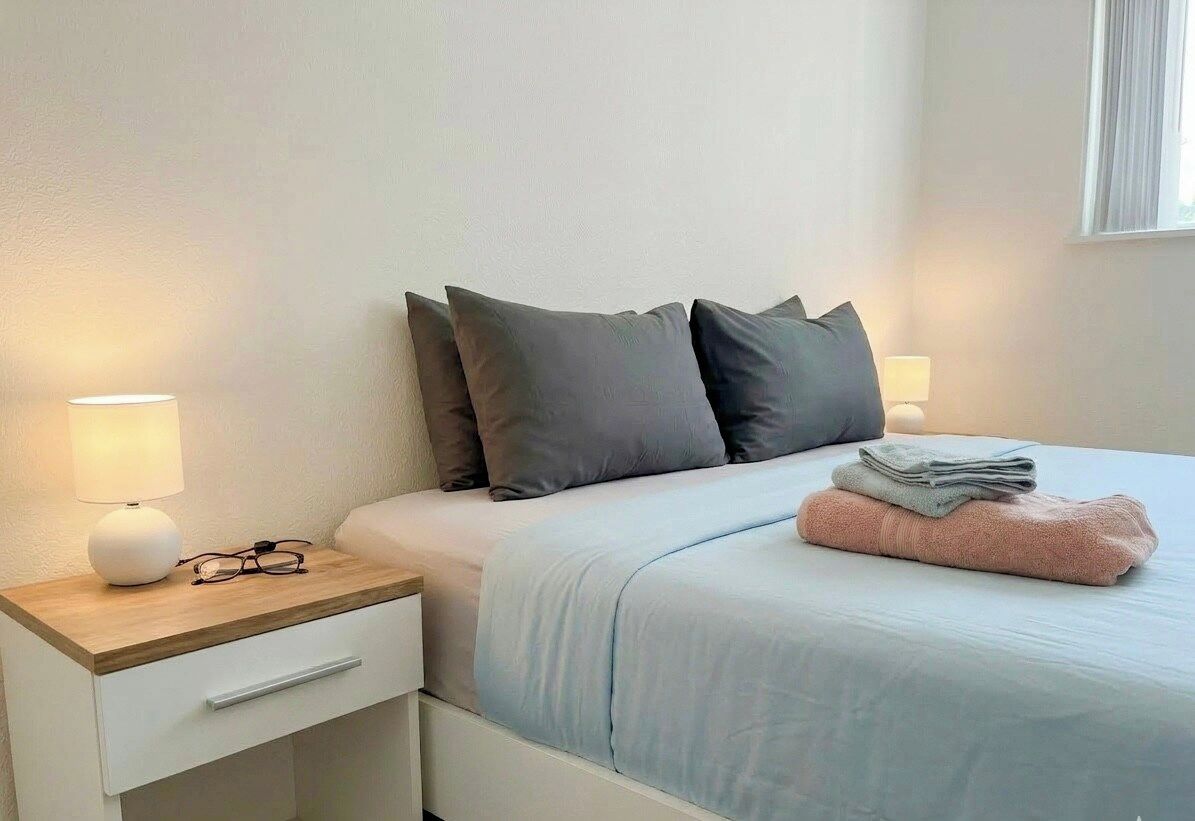 Un lit bien fait, avec des oreillers, une lampe de chevet, un tiroir et une serviette pliée posée sur le lit.