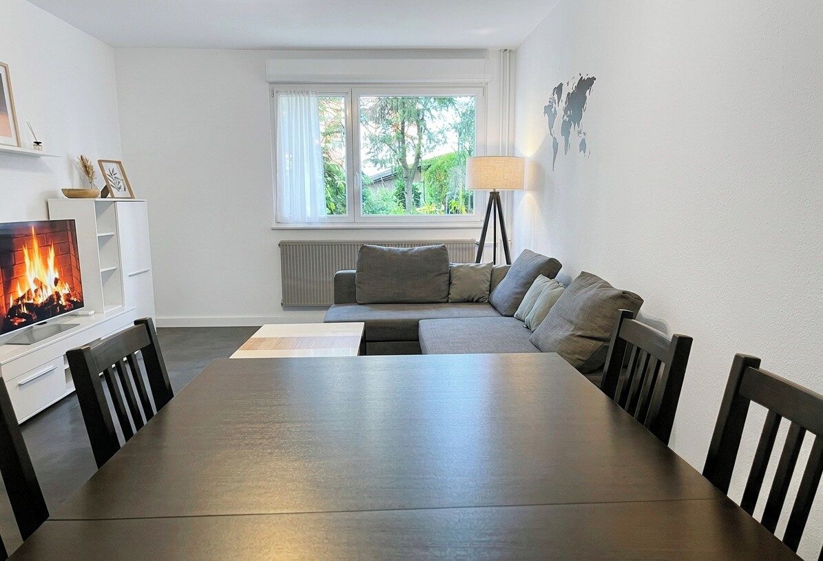 Una sala de estar moderna con chimenea, un sofá, una mesa de comedor y una ventana con vista a zonas verdes.