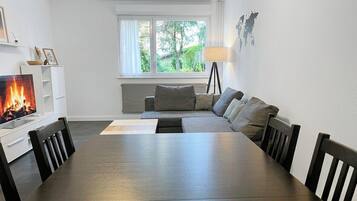 Una sala de estar moderna con chimenea, un sofá, una mesa de comedor y una ventana con vista a zonas verdes.