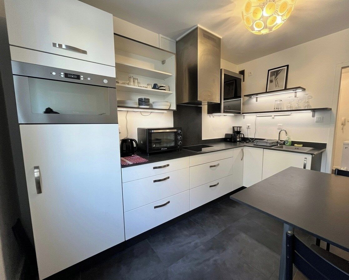 Una cucina moderna con mobili bianchi, forno integrato, microonde e macchina del caffè.