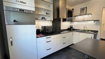 Una cucina moderna con mobili bianchi, forno integrato, microonde e macchina del caffè.