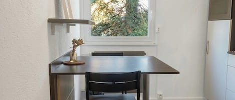 A compact kitchen with a dining table and chairs, a window with a view of trees, and built-in appliances.