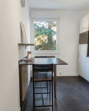 A compact kitchen with a dining table and chairs, a window with a view of trees, and built-in appliances.