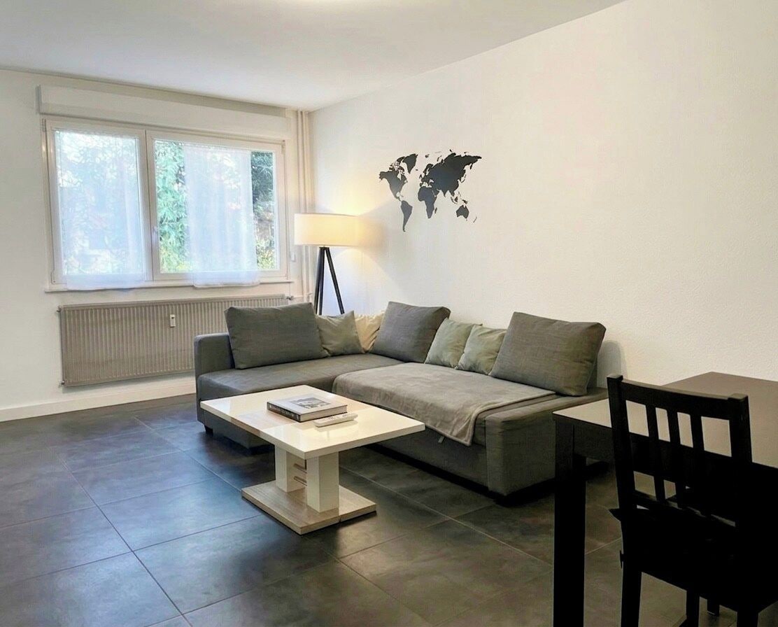 Uma sala de estar moderna com um sofá cinzento, uma mesa de centro branca, uma cadeira preta, um abajur e uma decoração de mapa-múndi na parede.