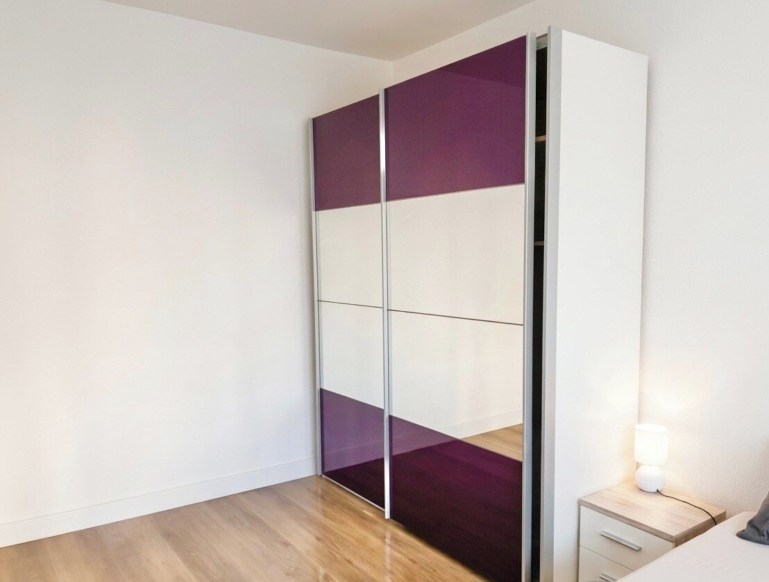 A room with a sliding wardrobe, a bedside table with a lamp, and a wooden floor.