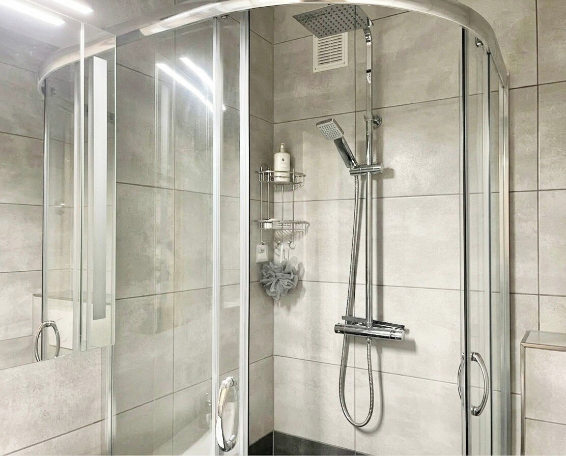 A glass-enclosed shower with a handheld showerhead and a wall-mounted faucet.