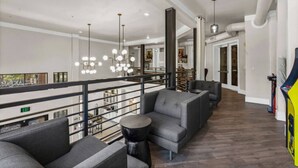 A spacious lounge area with a high ceiling, modern lighting fixtures, and a view of the upper floor.