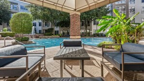A poolside area with lounge chairs, a table, and a covered seating area.