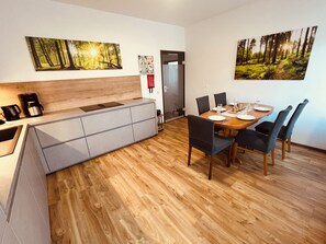 A modern kitchen with a built-in bench, a dining area with a wooden table and chairs, and two forest-themed wall art pieces. - WeserWaldGlück Vacation Rental - "A Little Getaway" - NEW in Wesertal for 4-5 people (Wesertal)