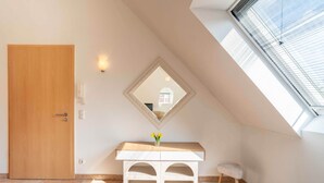 A room with a wooden door, a white console table with a mirror above it, a small stool, and a skylight. - Stylish Apartment | WiFi, Sky TV & Nespresso (Sobernheim)